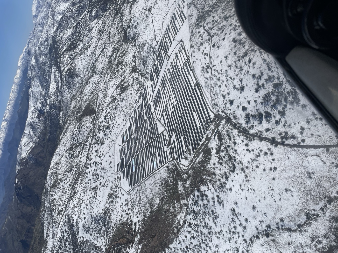 Vista aérea de una planta solar en plena cordillera nevada, fotografiada desde avioneta